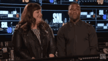 a man and a woman are standing in front of a screen that says snl on it