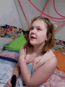 a little girl is laying on a bed with a remote control in her hand