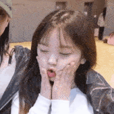 a little girl is making a face with her hands on her face .