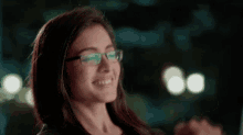 a woman wearing glasses is smiling and holding her hands together