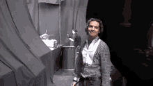 a man in a plaid shirt and suspenders is standing in a dark room