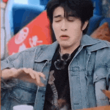 a man wearing a denim jacket and a black shirt is making a funny face .