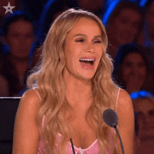 a woman in a pink top is laughing in front of a microphone with a star on it