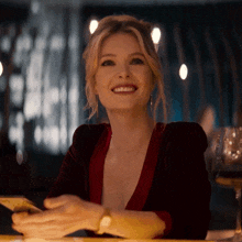 a woman in a red velvet top is smiling while holding a cell phone