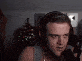 a man wearing headphones and a tank top is talking into a microphone in front of a christmas tree .