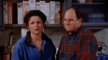 a man and a woman are standing next to each other in a kitchen with cereal boxes on the shelf behind them .
