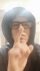 a young man wearing glasses and a hoodie is holding his nose .