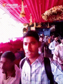 a man in a blue shirt is standing in front of a crowd of people and a sign that says video share chat
