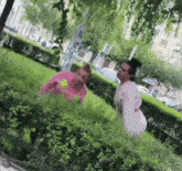 a woman in a pink shirt with a smiley face on it is standing next to a bush .