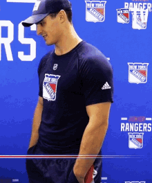 a man wearing a new york rangers shirt stands in front of a blue background