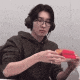 a young man wearing headphones and glasses is eating a sandwich .