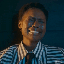 a woman in a striped shirt and tie is crying with tears coming out of her eyes .