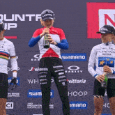 a woman is holding a bottle of wine in front of a banner that says shimano on it