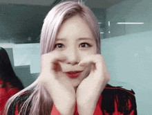 a girl with pink hair is making a heart shape with her hands