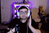 a man wearing headphones and glasses stands in front of a microphone in front of a shelf with stuffed animals on it
