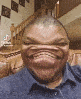 a man is making a funny face while sitting on a couch with stairs in the background .