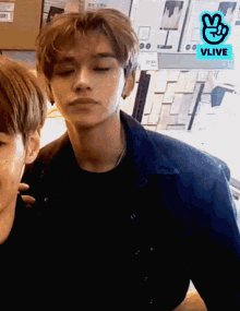 a man in a denim jacket is standing next to another man with a vlive logo on the bottom right