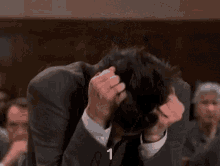 a man in a suit and tie is scratching his head with his hands .