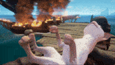a cartoon cat is laying on a dock with a burning ship in the background