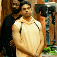 a man in a sleeveless hoodie stands next to another man in a black jacket