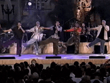 a group of men are dancing on a stage with a crowd watching