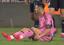 a soccer player in a pink adidas jersey sits on the field
