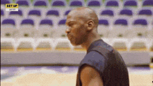 a bald man is standing on a basketball court in front of a row of empty seats .