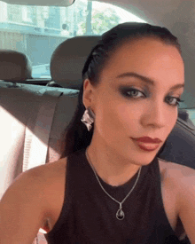 a woman wearing a necklace and earrings is taking a selfie in the back seat of a car