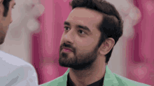 a man with a beard wearing a green jacket looks to his left