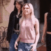 a woman in a pink tank top and blue jeans is walking next to two other women .