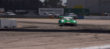 a green race car is driving down a track with a weathertech sign in the background