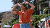 a man in a red shirt and blue jeans is standing on a beach with his arms outstretched