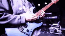 a person is playing a blue electric guitar with a hoodie on