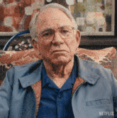 an older man wearing glasses and a blue jacket is sitting in a chair with a netflix logo on the bottom