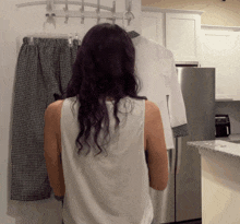 a woman in a white tank top is standing in front of a clothes rack