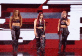 three women are standing next to each other on a stage and one is singing into a microphone .