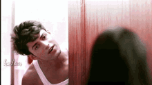 a man in a white tank top looks at his reflection in a mirror