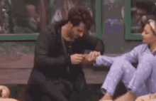 a man is putting a ring on a woman 's finger while they are sitting on a bench .