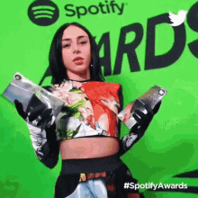 a woman holding two trophies in front of a green spotify sign
