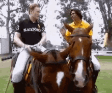 two men are riding horses and one of them is wearing a black shirt that says black x white