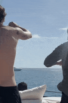 a man without a shirt is standing on a boat looking at the ocean