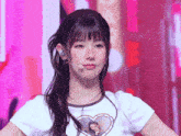 a girl wearing a white shirt with a heart on it looks at the camera
