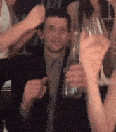 a man in a suit is surrounded by people holding wine glasses and a bottle