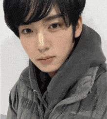 a young man wearing a grey jacket with a hood is looking at the camera