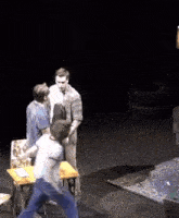 a group of men are standing around a table on a stage in a dark room .