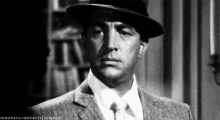 a man in a suit and tie is wearing a hat and looking at the camera .