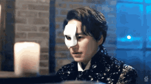 a man wearing a mask is sitting at a table with a candle .