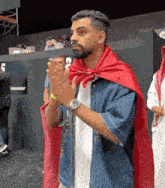 a man wearing a red cape is clapping his hands while standing in front of a crowd .