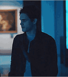 a man is standing in a dark room in front of a painting .