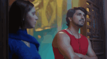a man in a red tank top stands next to a woman in a blue shirt